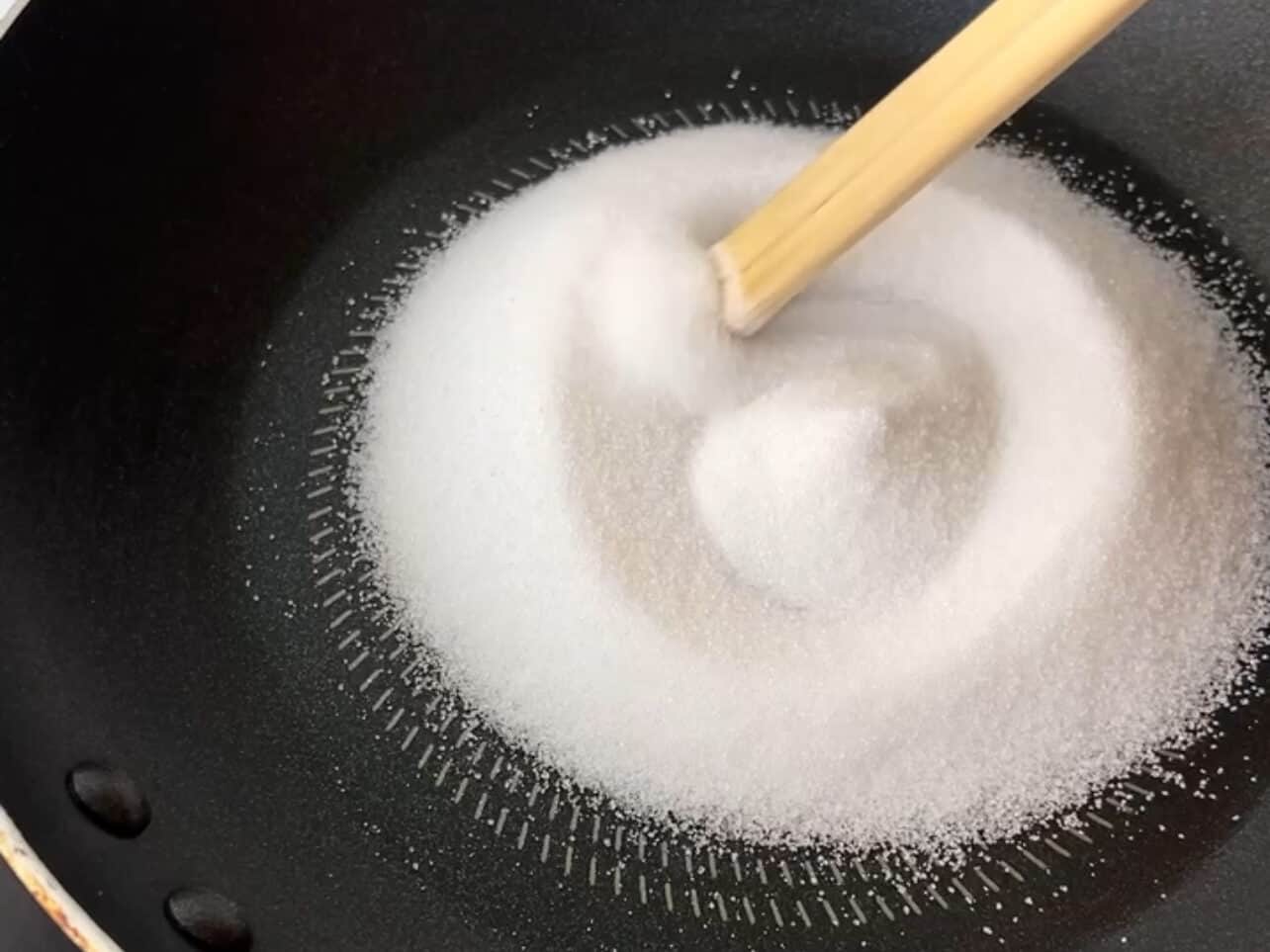 Adding sugar to pan or ladle. Stir with chopsticks as it melts.