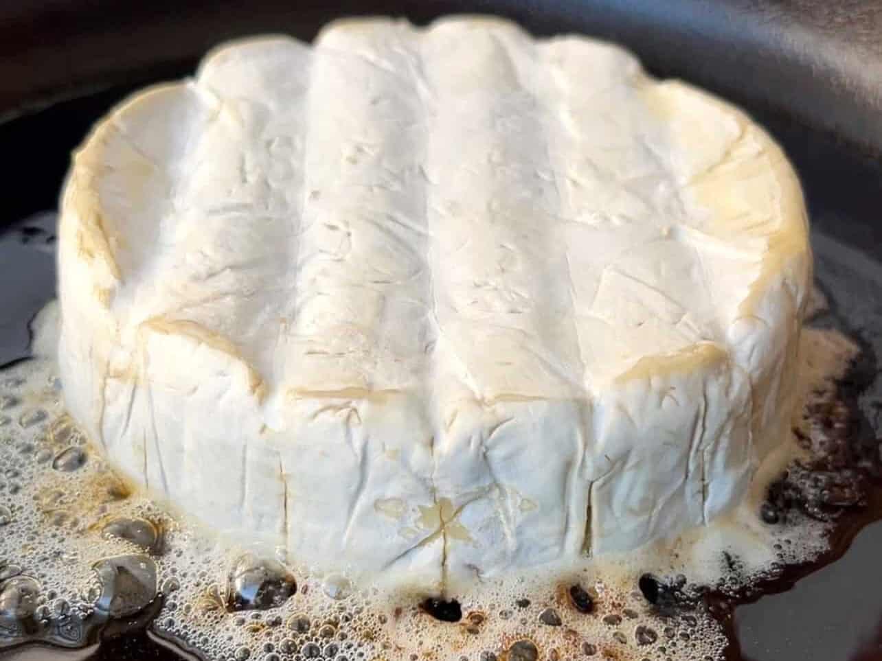 brown scored brie on cast iron pan