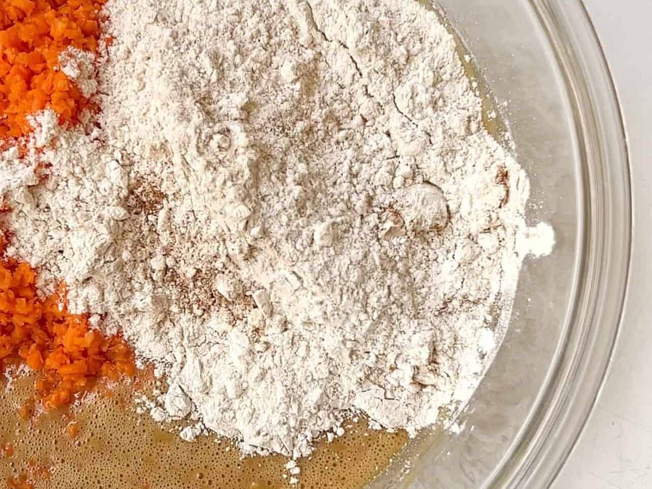 adding carrots and dry ingredients to wet carrot cake batter