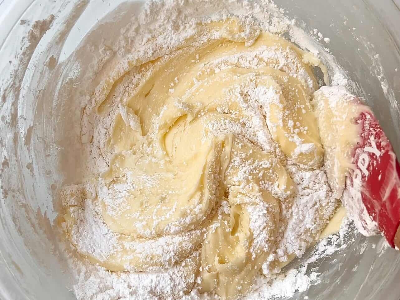 mixing and stirring sifted powdered sugar into lemon raspberry cupcake batter