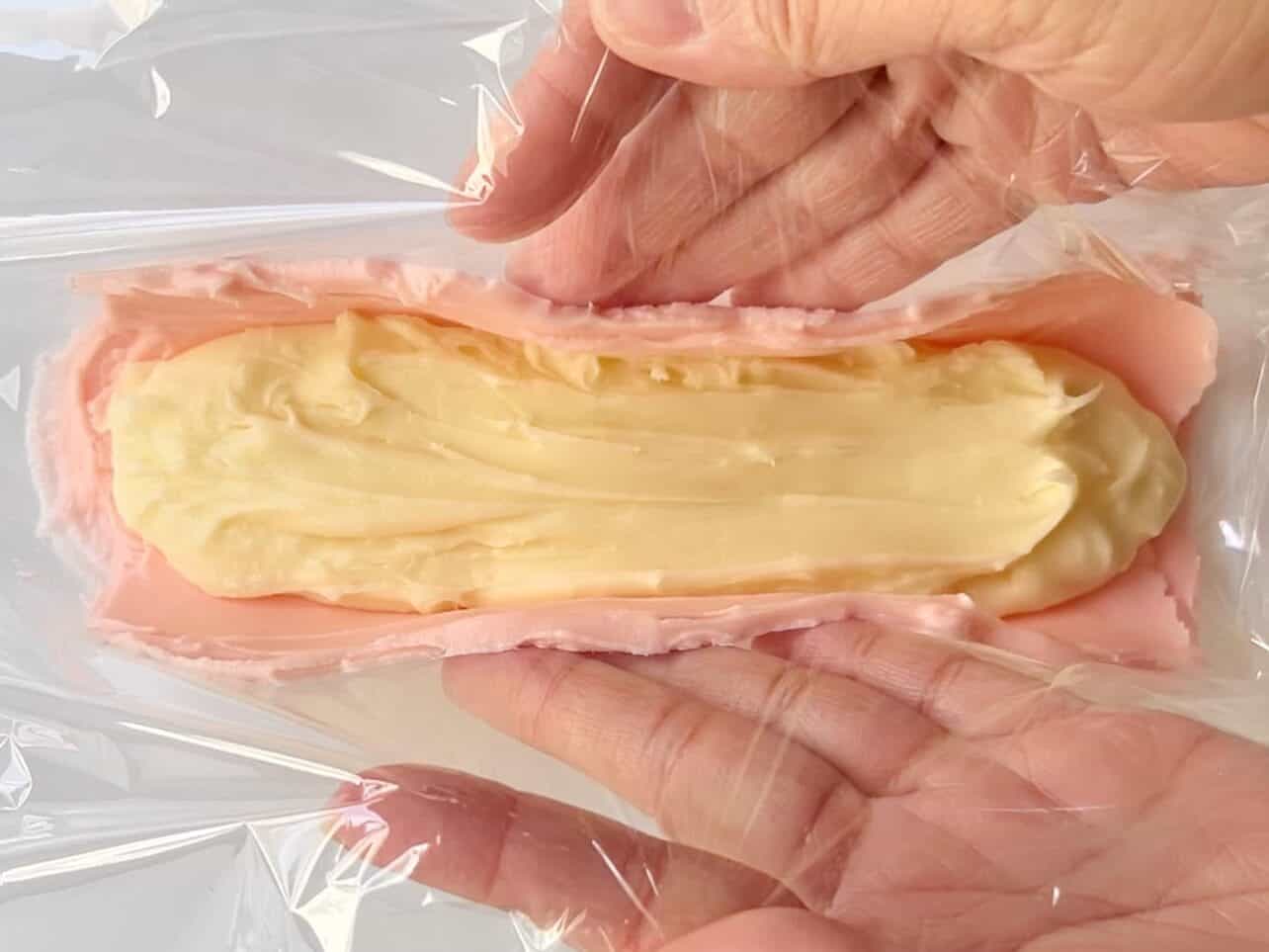 wrapping pink frosting to encase yellow frosting in the middle using cling wrap