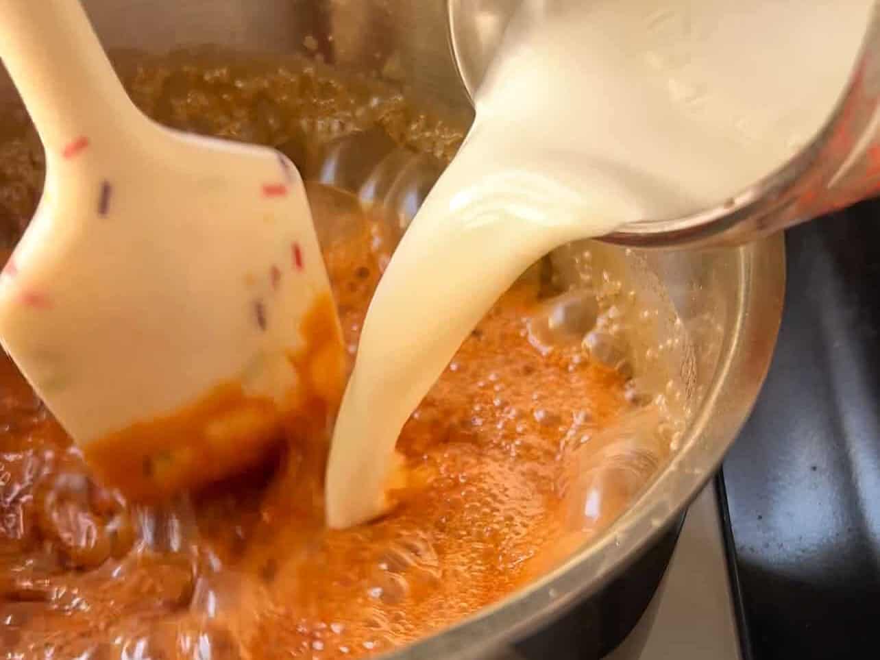 pouring heavy cream into melted sugar to make homemade caramel