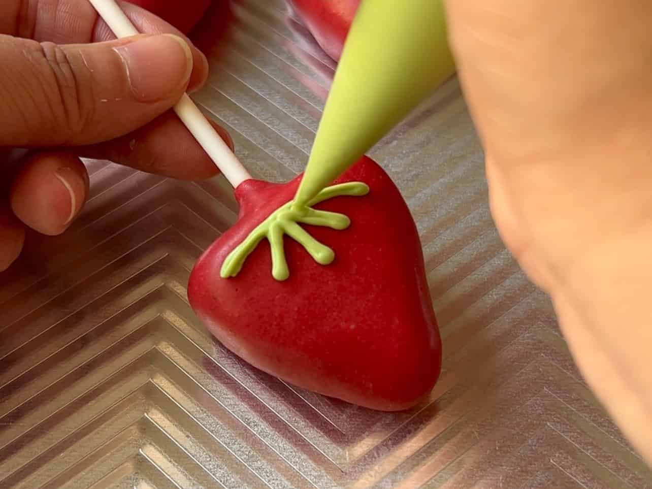 use melted green candy melts to draw strawberry leaves using piping bag