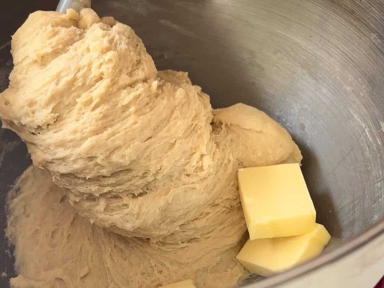 adding softened butter to shaggy brioche dough in a stand mixer