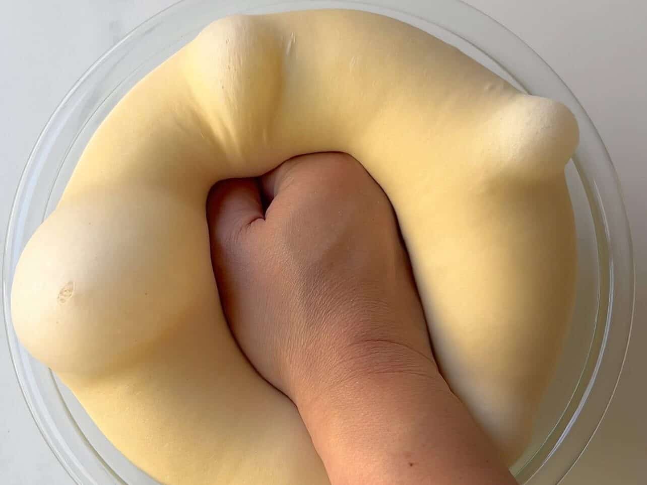 punching brioche dough in a bowl after first rise