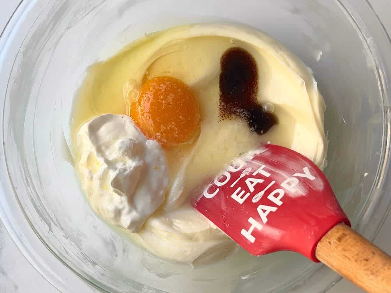 adding egg, sour cream, vanilla bean paste, and salt to sweetened cream cream for cheesecake filling