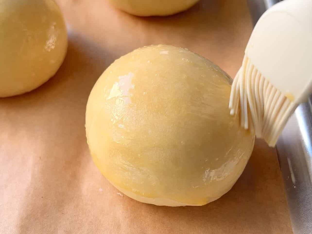 brushing egg wash on proofed brioche rolls on baking sheet
