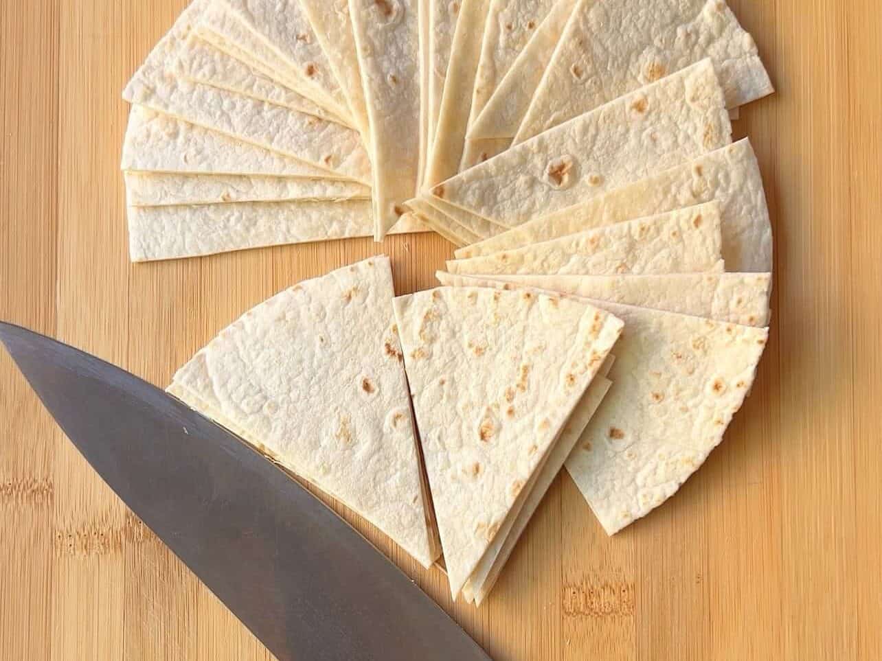 flour tortillas sliced with a knife into triangles on a cutting board