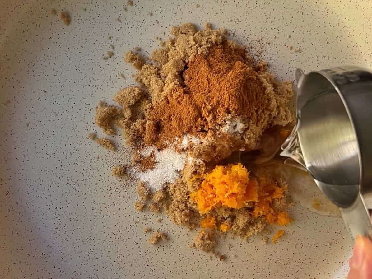 preparing brown sugar, salt, cinnamon, orange zest, vanilla, and water in skillet to make candied pecan glaze