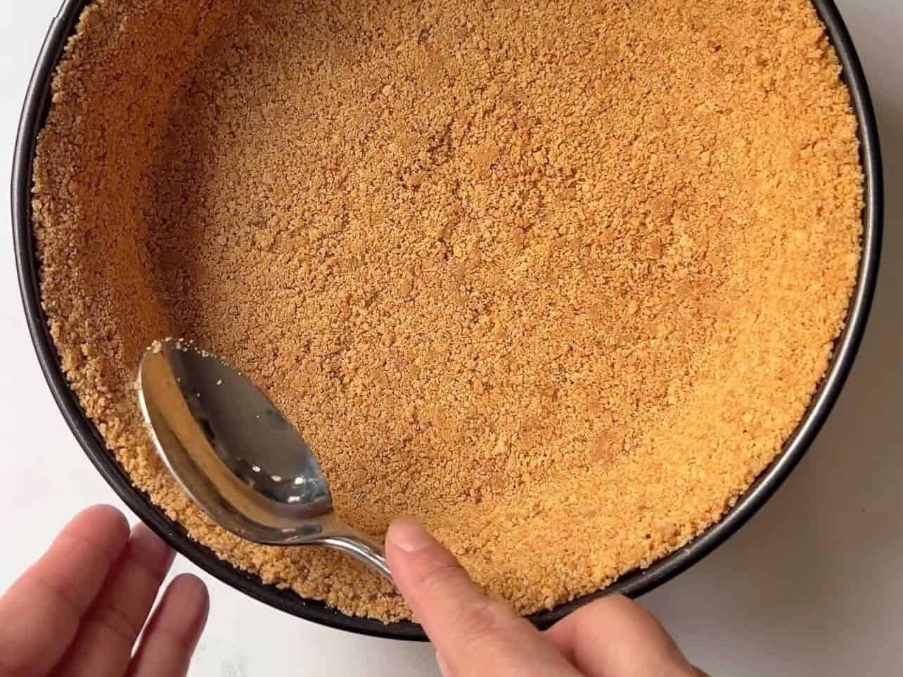 spreading cheesecake graham cracker crust evenly in springform pan