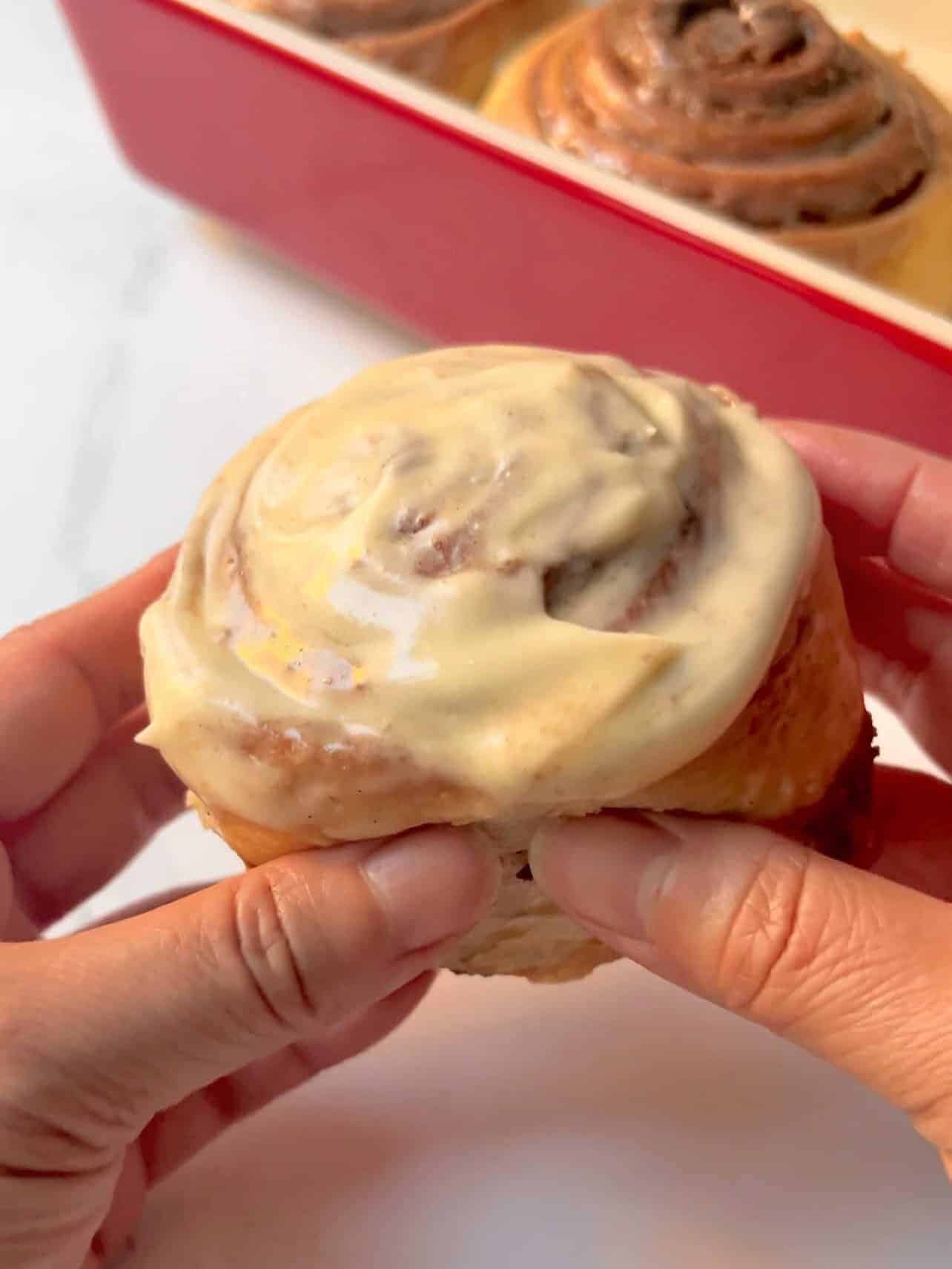 Cinnabon copycat cinnamon roll slathered with frosting held in hand