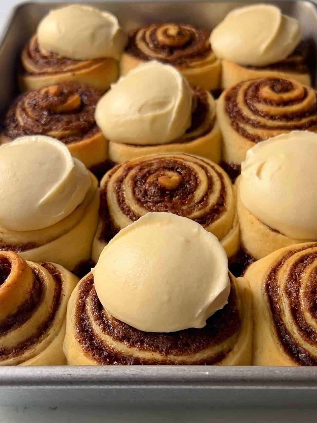 Cinnabon copycat cinnamon rolls baked in pan with dollops of cream cheese frosting
