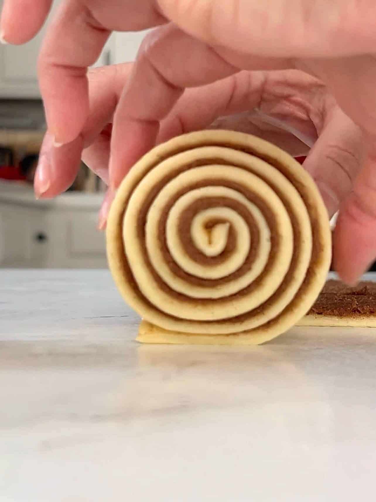 Cinnabon copycat cinnamon roll dough being cut into strips and rolled into spiral